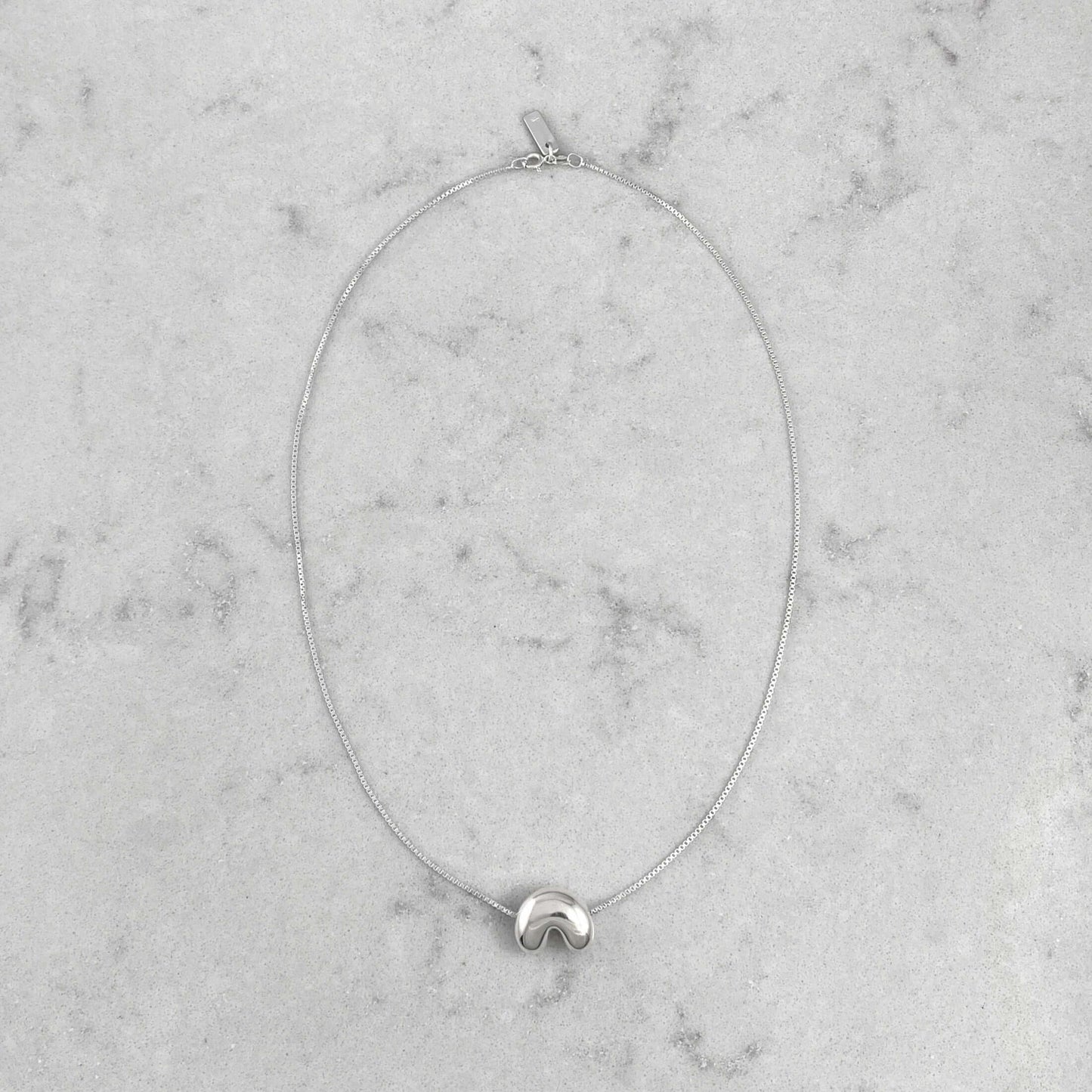 Product photo of a silver necklace by Aur Studio. On a marble plate